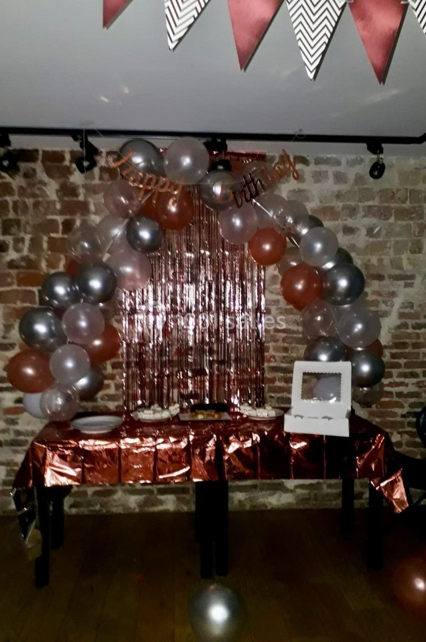 Location salle Paris 11 (Paris) - Les Rendez-vous #15 Décoration d'anniversaire avec ballons argentés et cuivrés, guirlande et table dressée devant un mur de briques.