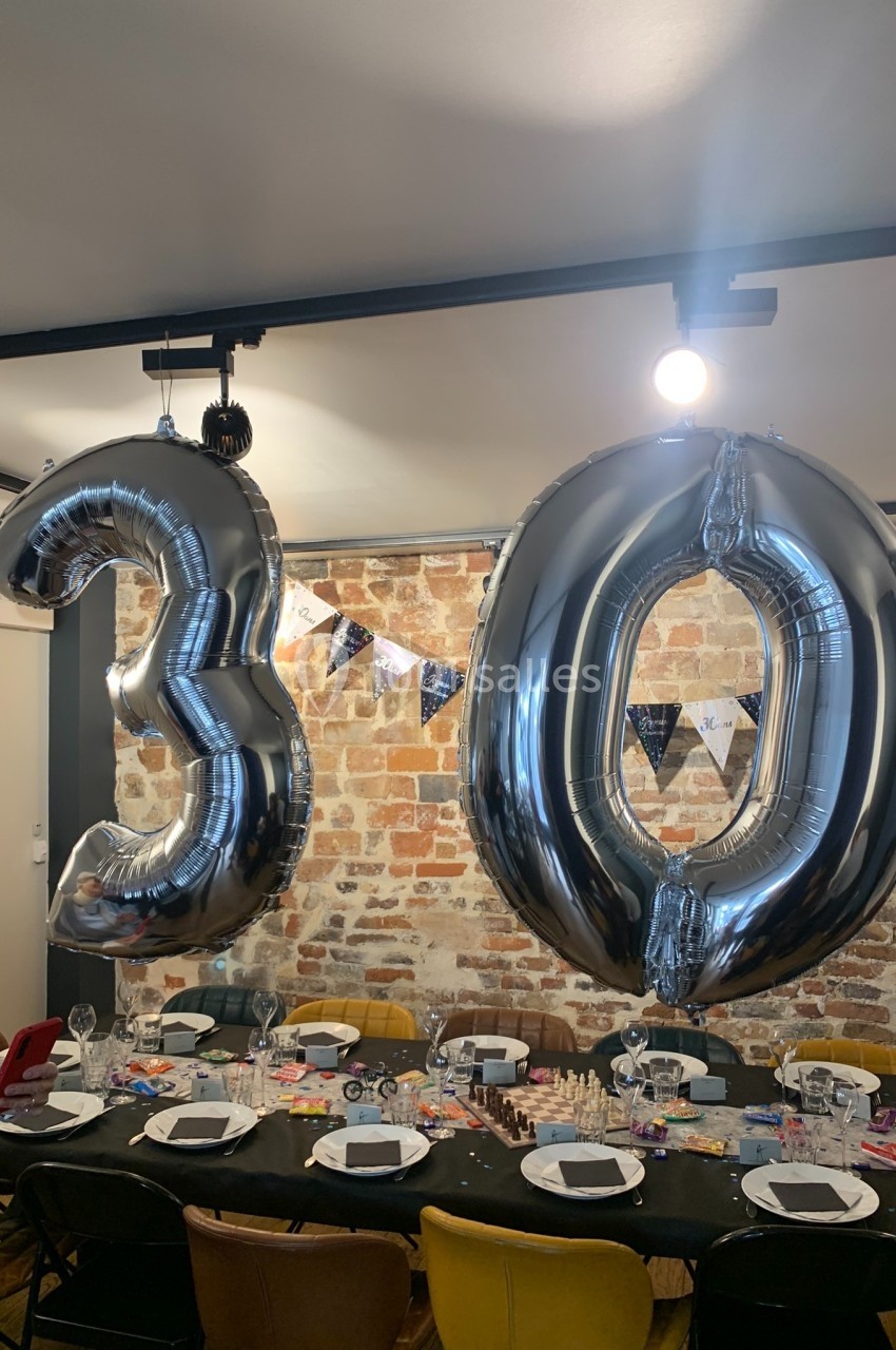 Location salle Paris 11 (Paris) - Les Rendez-vous #13 Ballons argentés formant le chiffre 30 suspendus au-dessus d'une table décorée pour une fête dans une pièce en briques…