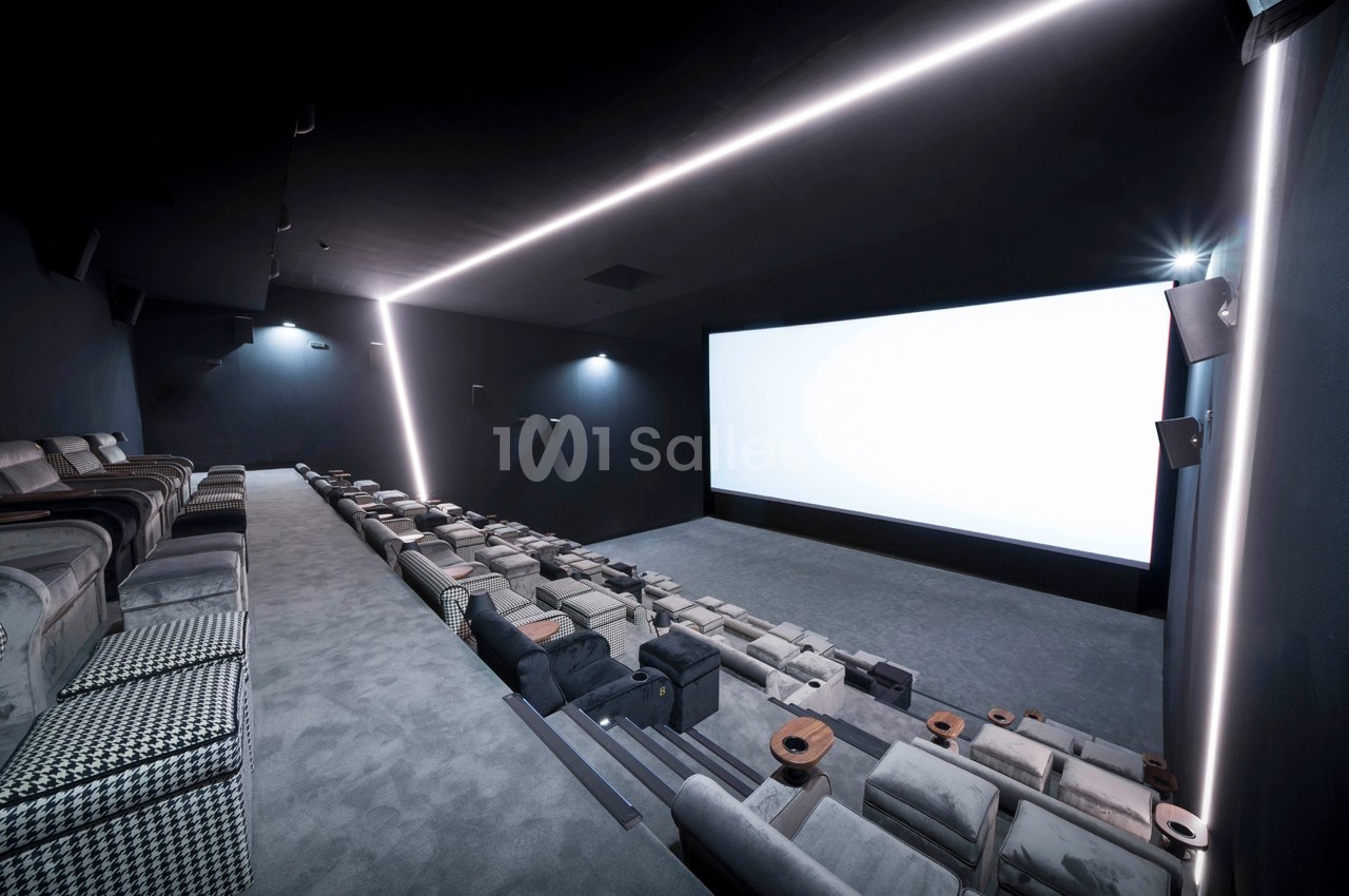 Salle de cinéma moderne avec sièges confortables en gradins, éclairage tamisé et grand écran blanc.