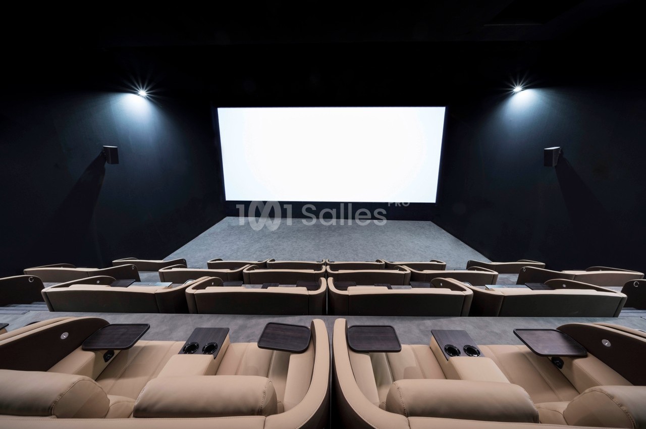 Salle de cinéma moderne avec des fauteuils en cuir beige et un grand écran blanc allumé.