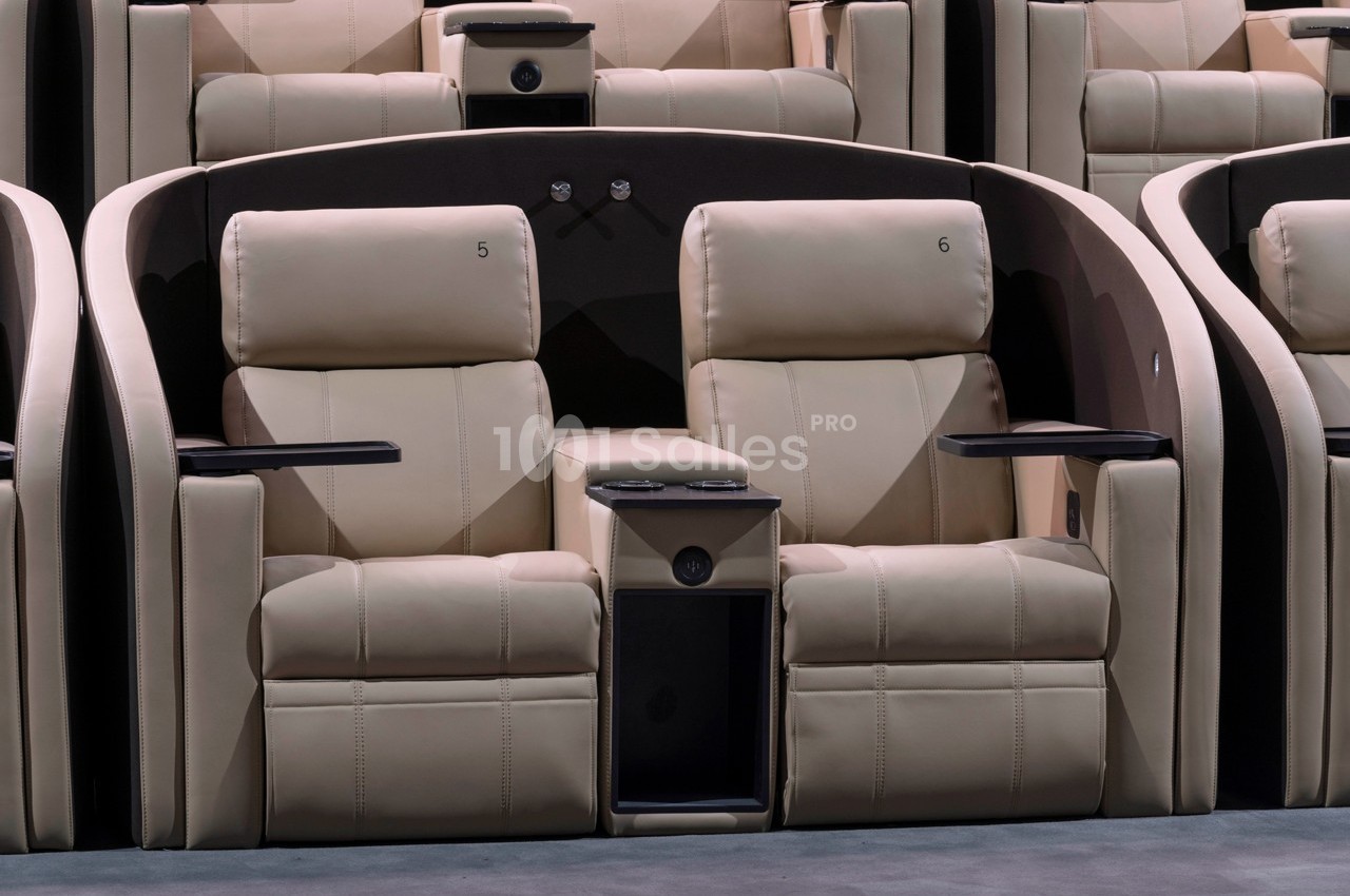 Deux fauteuils de cinéma en cuir beige avec accoudoirs, porte-gobelets et séparation centrale.
