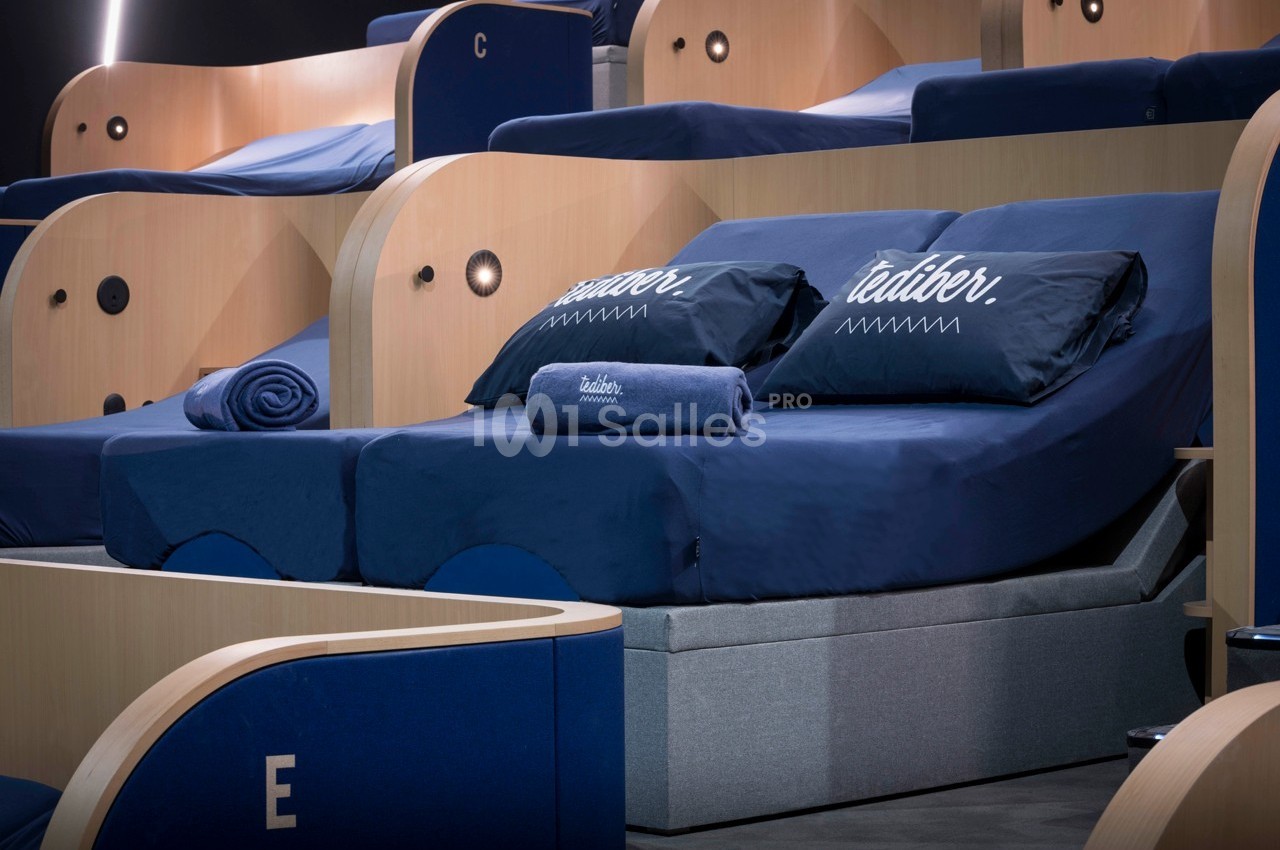 Deux lits inclinables avec draps et coussins bleus, accompagnés de serviettes, dans un espace moderne en bois.