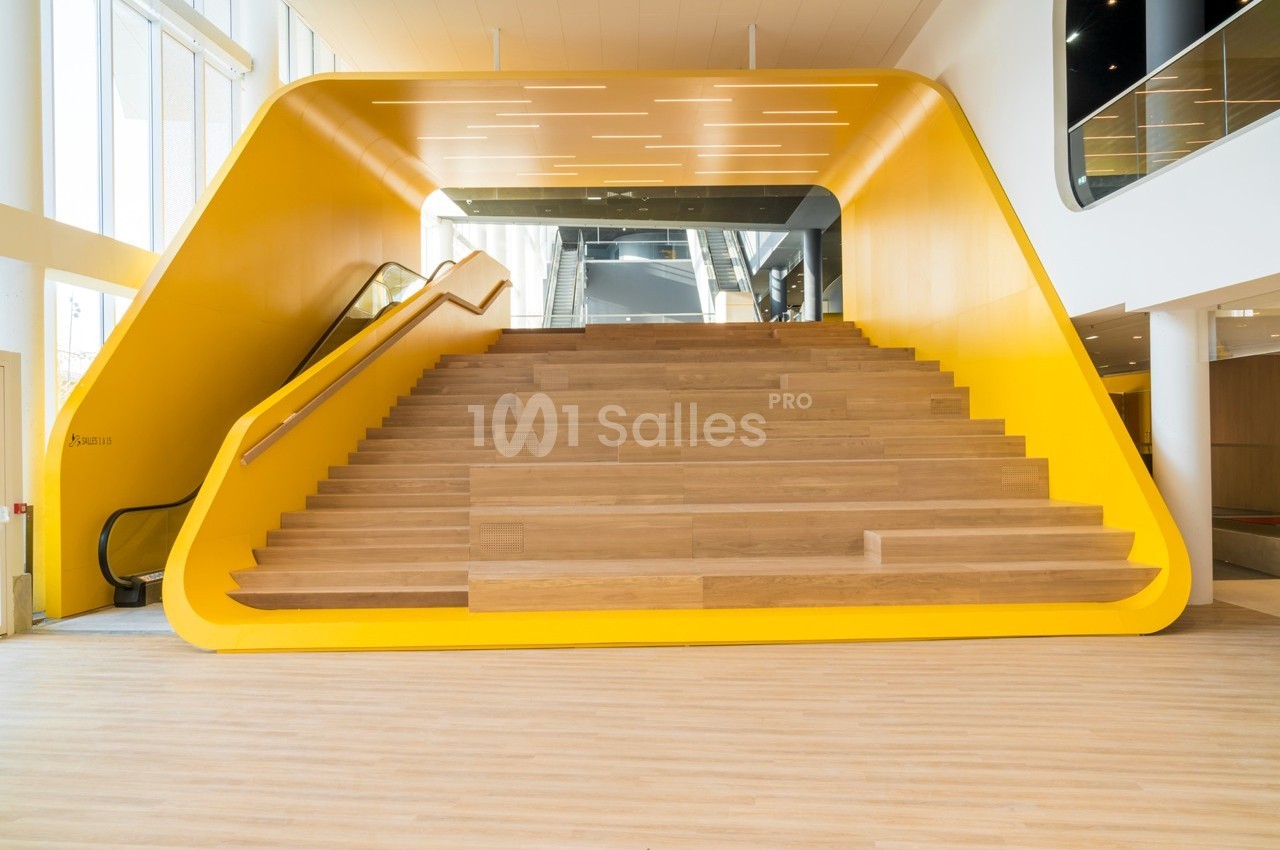 Escalier en bois entouré d'une structure jaune vif dans un espace intérieur moderne et lumineux.