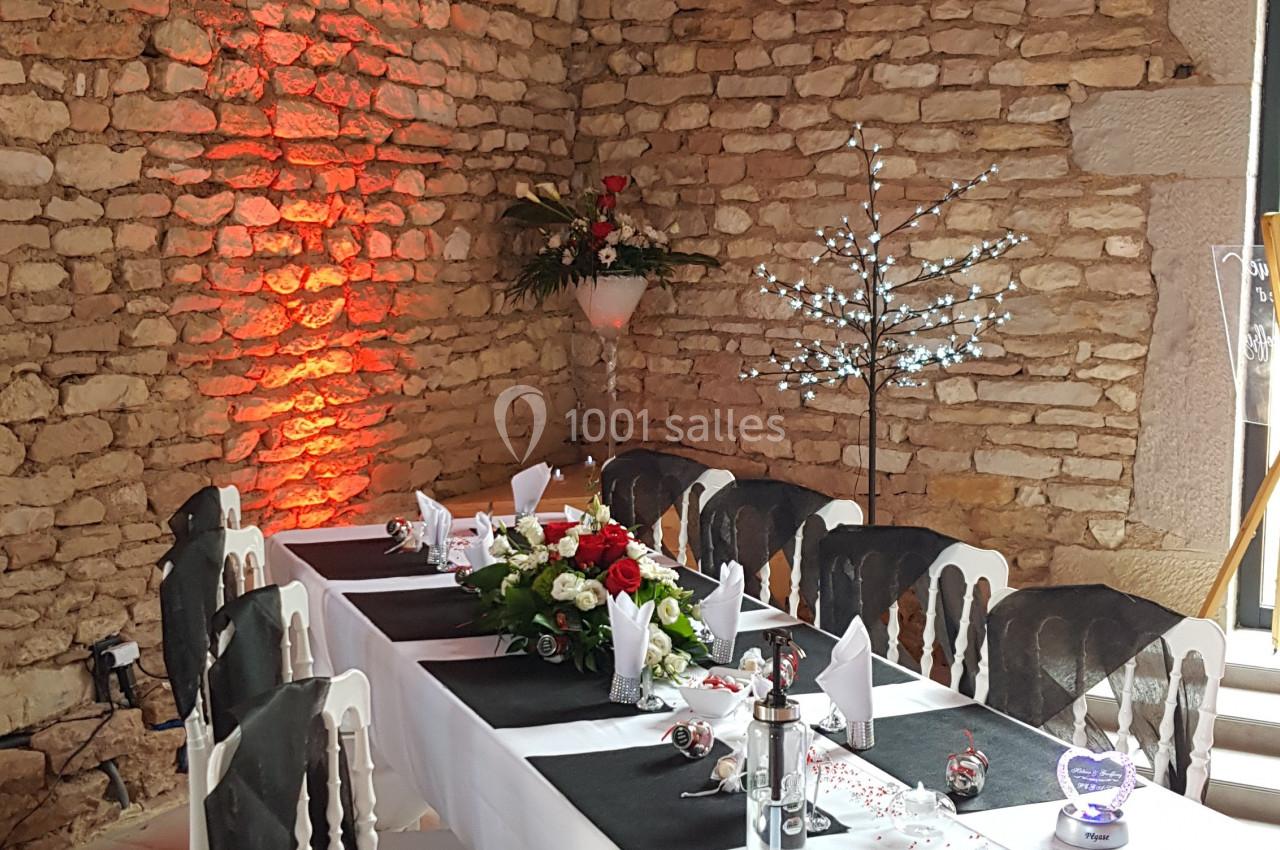 Table de réception décorée avec nappes noires et blanches, fleurs et bougies, dans une salle aux murs en pierre.
