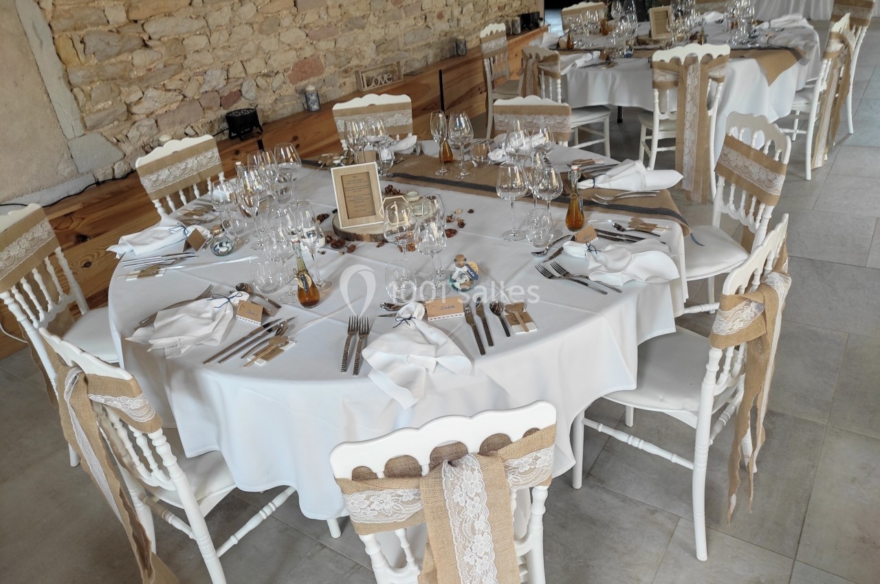 Tables rondes décorées pour un événement, avec nappes blanches, chaises ornées de rubans et vaisselle élégante.