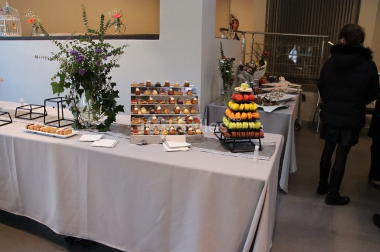 Table garnie de desserts variés, dont des macarons et des pâtisseries, avec des décorations florales en arrière-plan.