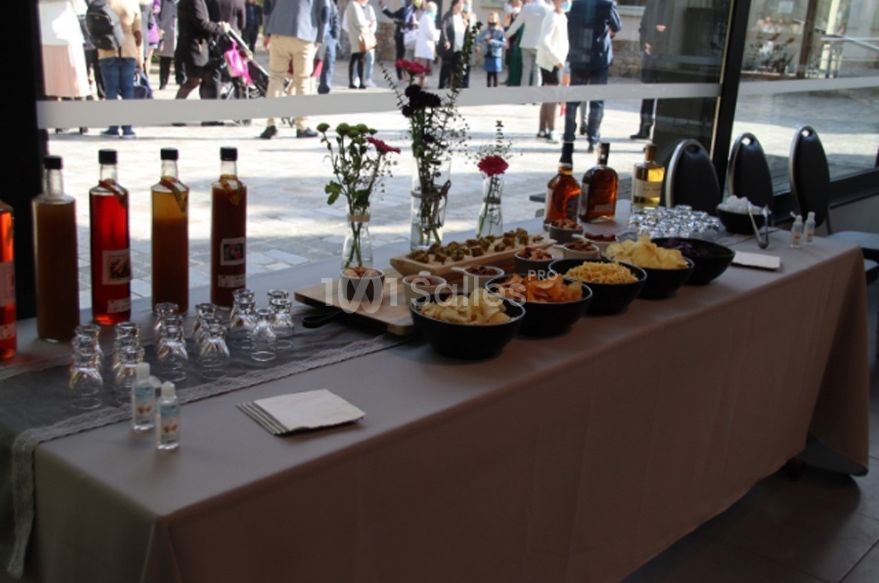 Table dressée avec des boissons, des verres, des bols de snacks et des fleurs, dans un espace lumineux avec vue extérieure.