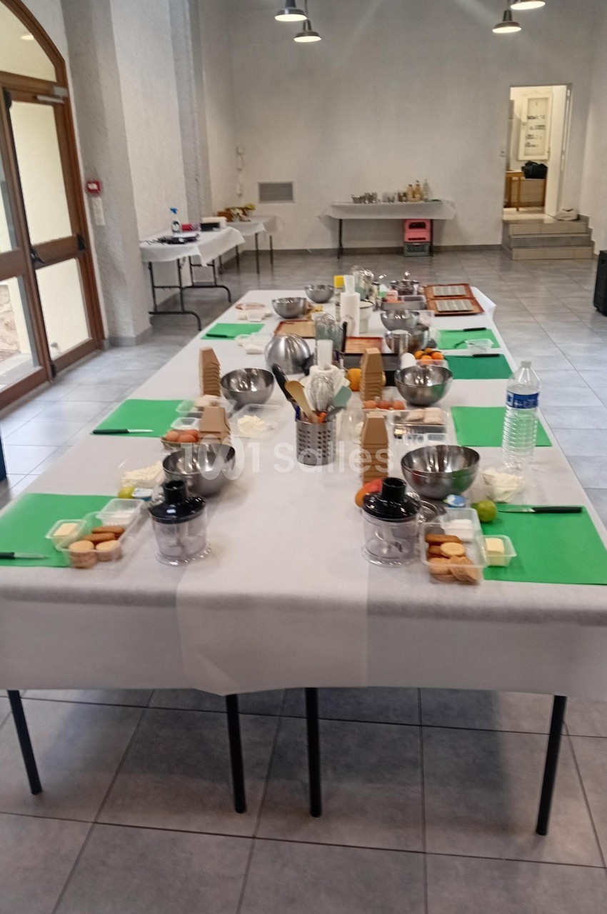 Tables dressées avec des ustensiles de cuisine, planches vertes et ingrédients, dans une salle lumineuse.