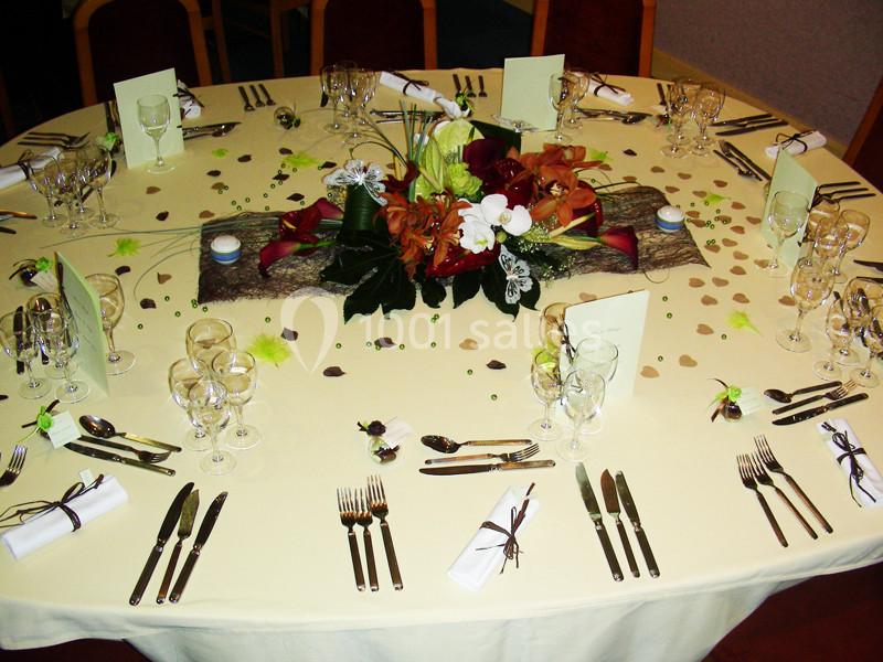 Table ronde dressée pour un repas formel avec nappes claires, couverts alignés, verres et décoration florale centrale.
