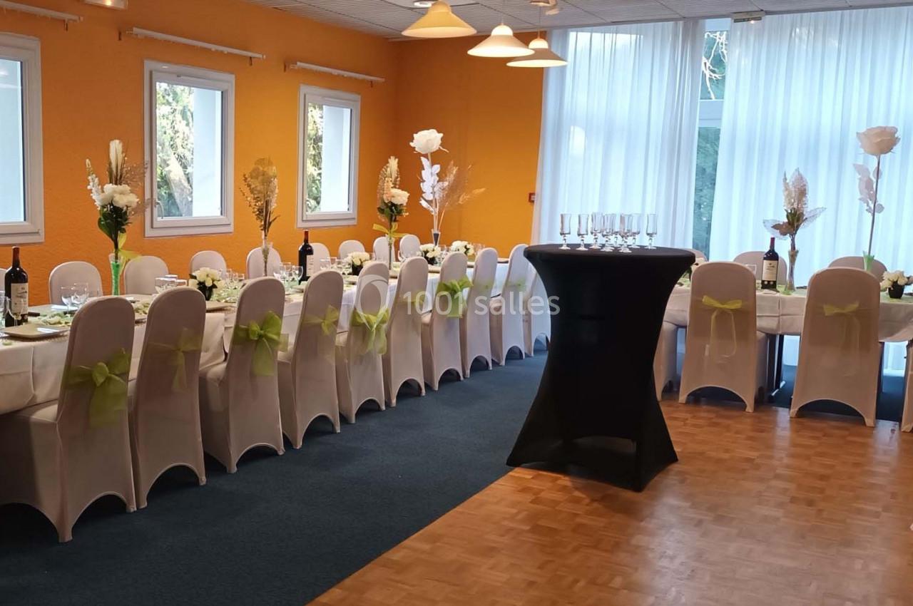 Salle décorée pour un événement avec tables dressées, chaises ornées de nœuds verts et un buffet central.