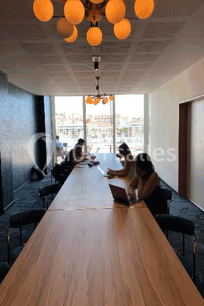 Des personnes travaillent sur des ordinateurs portables autour d'une grande table dans une salle lumineuse avec vue sur l…