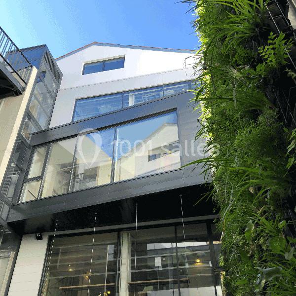Façade moderne d'un bâtiment avec grandes baies vitrées et mur végétal sur le côté droit.