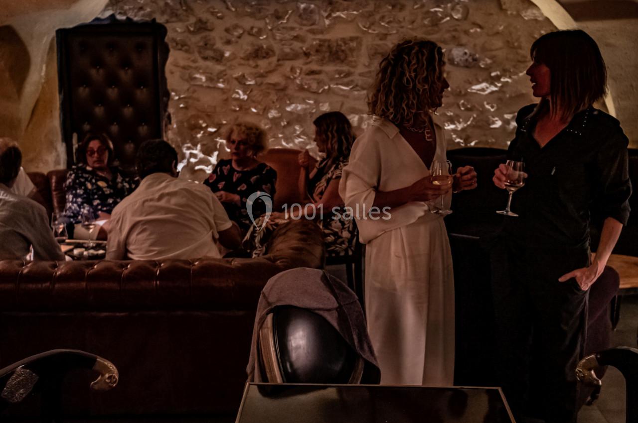 Des personnes discutent et partagent un moment convivial dans un salon à l'éclairage tamisé, avec murs en pierre apparente.