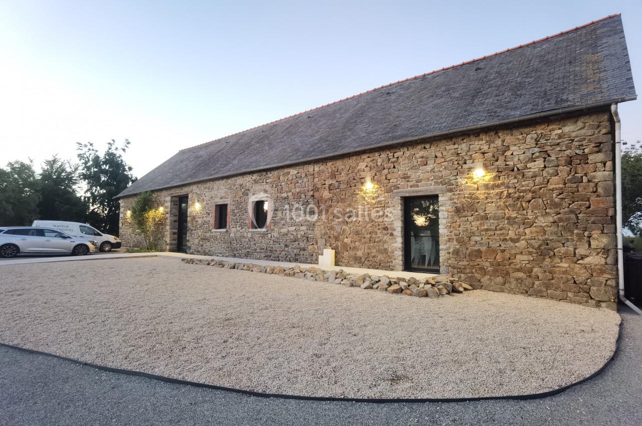 Location salle Domagné (Ille-et-Vilaine) - Domaine de Neuville #2 Façade d'une maison en pierre avec toit en ardoise, éclairée par des appliques murales, entourée de gravier.