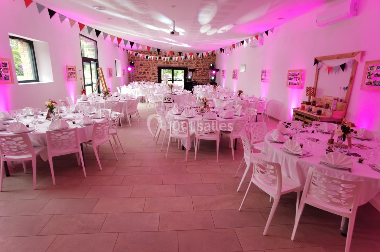 Location salle Domagné (Ille-et-Vilaine) - Domaine de Neuville #14 Salle décorée pour un événement avec tables rondes dressées, guirlandes colorées et éclairage rose.