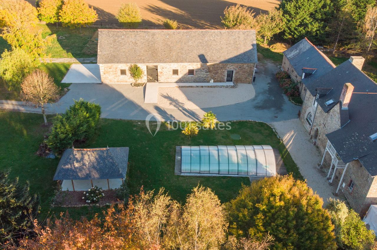 Location salle Domagné (Ille-et-Vilaine) - Domaine de Neuville #5 Vue aérienne d'une propriété avec bâtiments en pierre, piscine couverte et jardin arboré en automne.