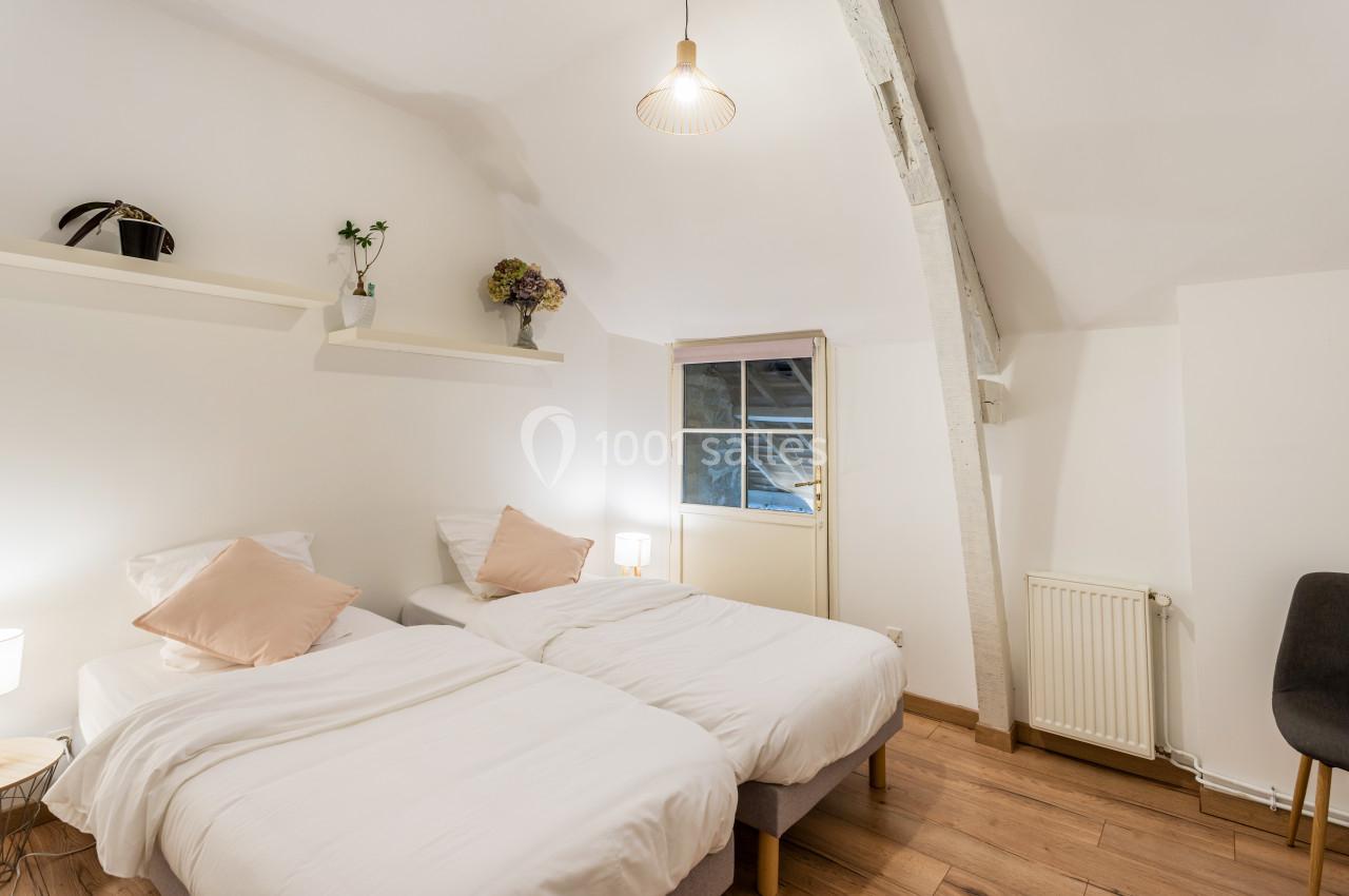 Location salle Domagné (Ille-et-Vilaine) - Domaine de Neuville #9 Deux lits simples avec draps blancs dans une chambre lumineuse, décorée de plantes et d'une fenêtre en arrière-plan.