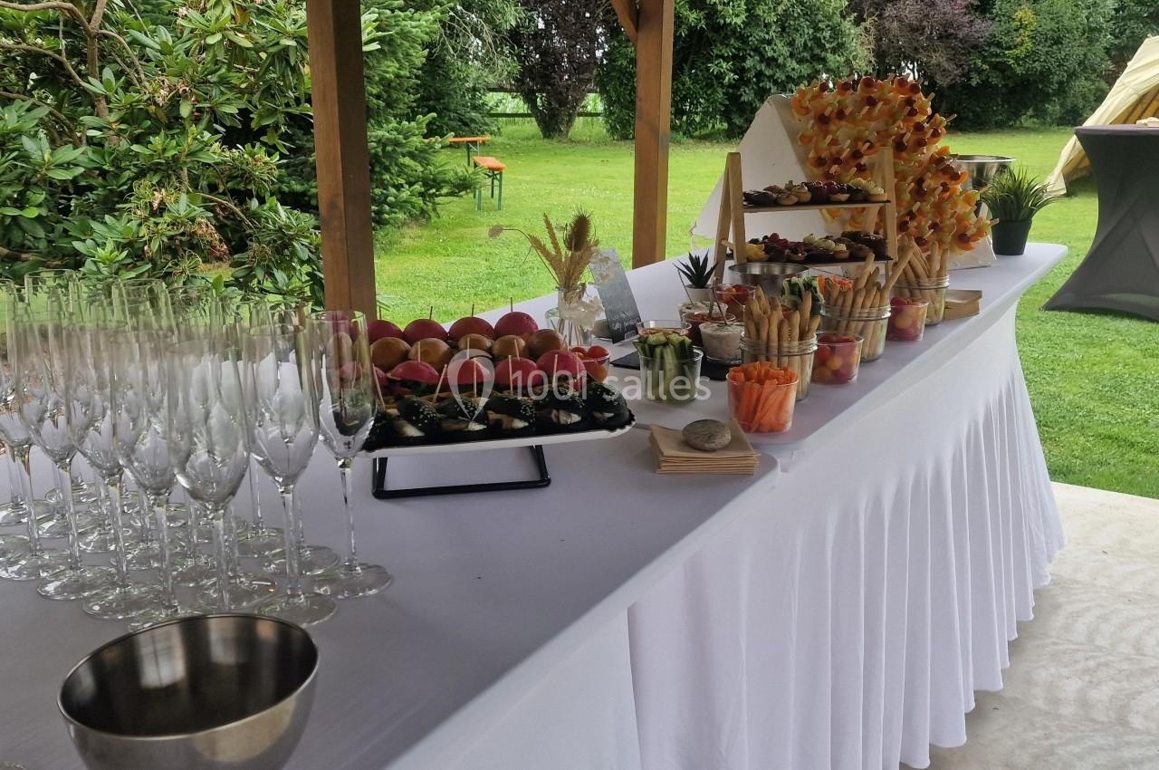 Location salle Domagné (Ille-et-Vilaine) - Domaine de Neuville #16 Table dressée en extérieur avec verrerie, amuse-bouches variés et décorations végétales sous un auvent.
