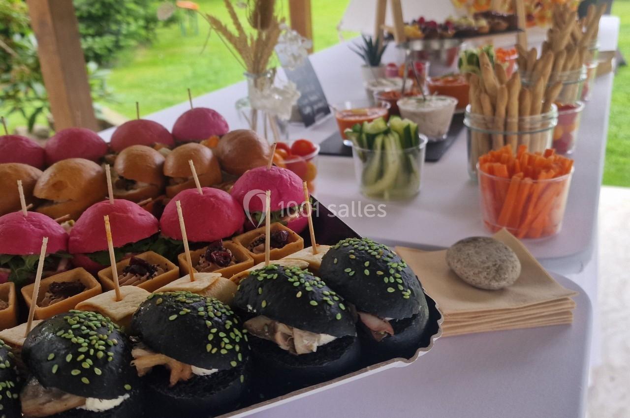 Location salle Domagné (Ille-et-Vilaine) - Domaine de Neuville #13 Plateau de mini-burgers colorés et verrines de légumes disposés sur une table pour un buffet en extérieur.