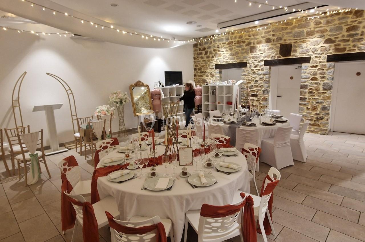 Location salle Domagné (Ille-et-Vilaine) - Domaine de Neuville #19 Salle de réception décorée avec des tables rondes, nappes blanches, chaises ornées de rubans rouges et guirlandes lumineuses.