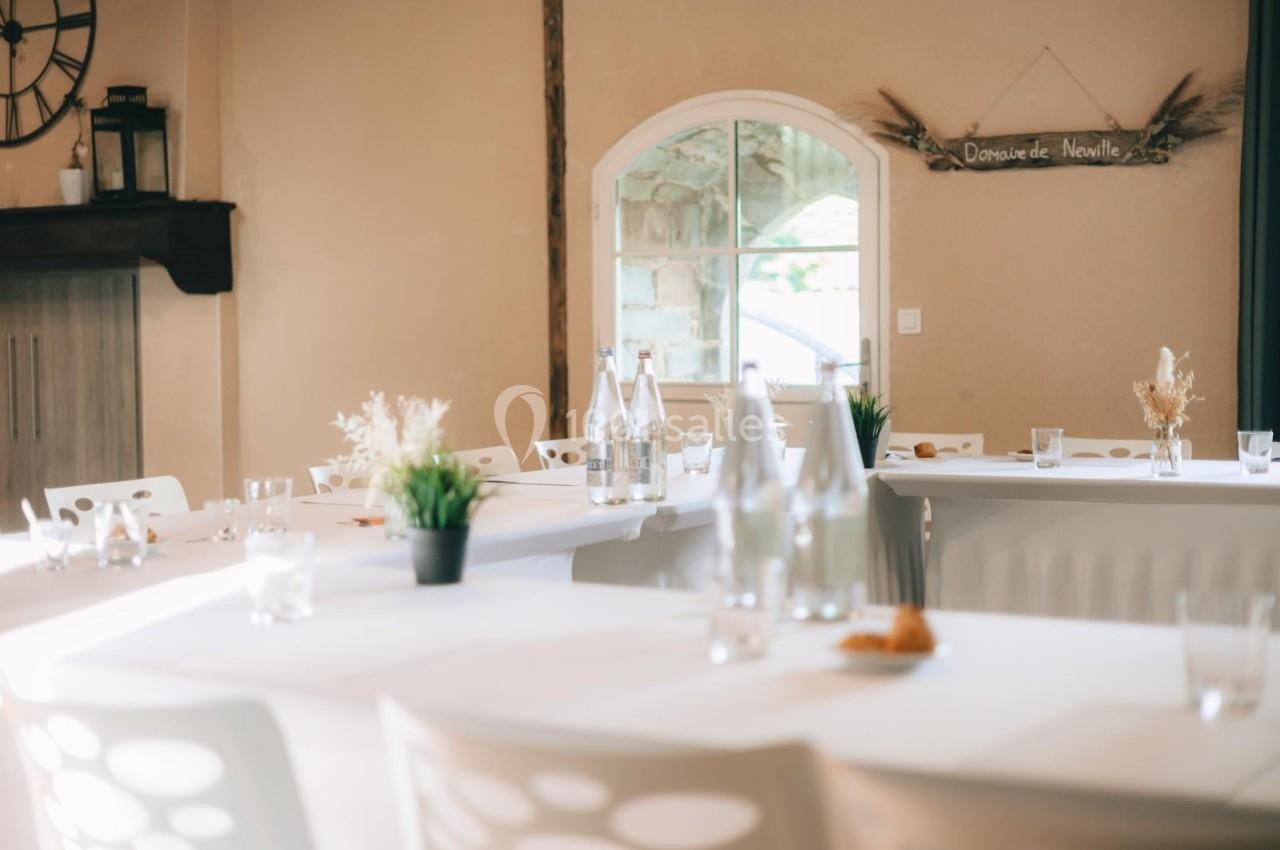 Location salle Domagné (Ille-et-Vilaine) - Domaine de Neuville #11 Salle lumineuse avec tables blanches décorées de plantes et bouteilles, près d'une fenêtre et d'un panneau mural.