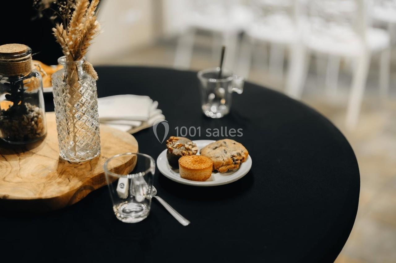 Location salle Domagné (Ille-et-Vilaine) - Domaine de Neuville #20 Assiette contenant des cookies et un petit gâteau sur une table noire, avec des verres et un vase décoratif à proximité.