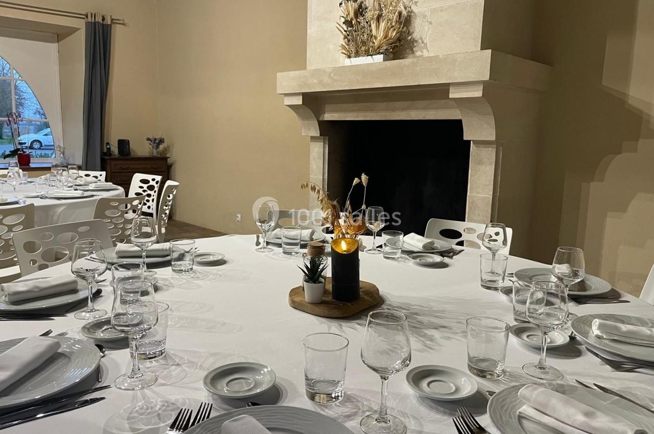 Location salle Domagné (Ille-et-Vilaine) - Domaine de Neuville #15 Table dressée avec nappes blanches, vaisselle élégante et centre de table décoratif, dans une salle avec cheminée en pierre.