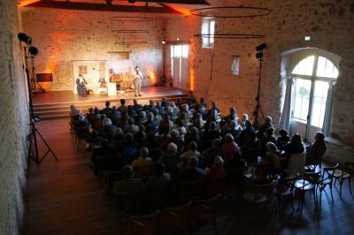 Miniature Location salle Cezais (Vendée) - Château de la Cressonnière #44 Un homme debout, bras ouverts, s'exprime devant un mur en pierre, avec une chaise en bois à côté de lui.