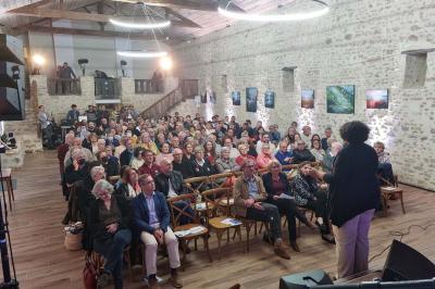 Miniature Location salle Cezais (Vendée) - Château de la Cressonnière #45 Un homme debout, bras ouverts, s'exprime devant un mur en pierre, avec une chaise en bois à côté de lui.