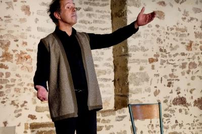 Miniature Location salle Cezais (Vendée) - Château de la Cressonnière #49 Un homme debout, bras ouverts, s'exprime devant un mur en pierre, avec une chaise en bois à côté de lui.