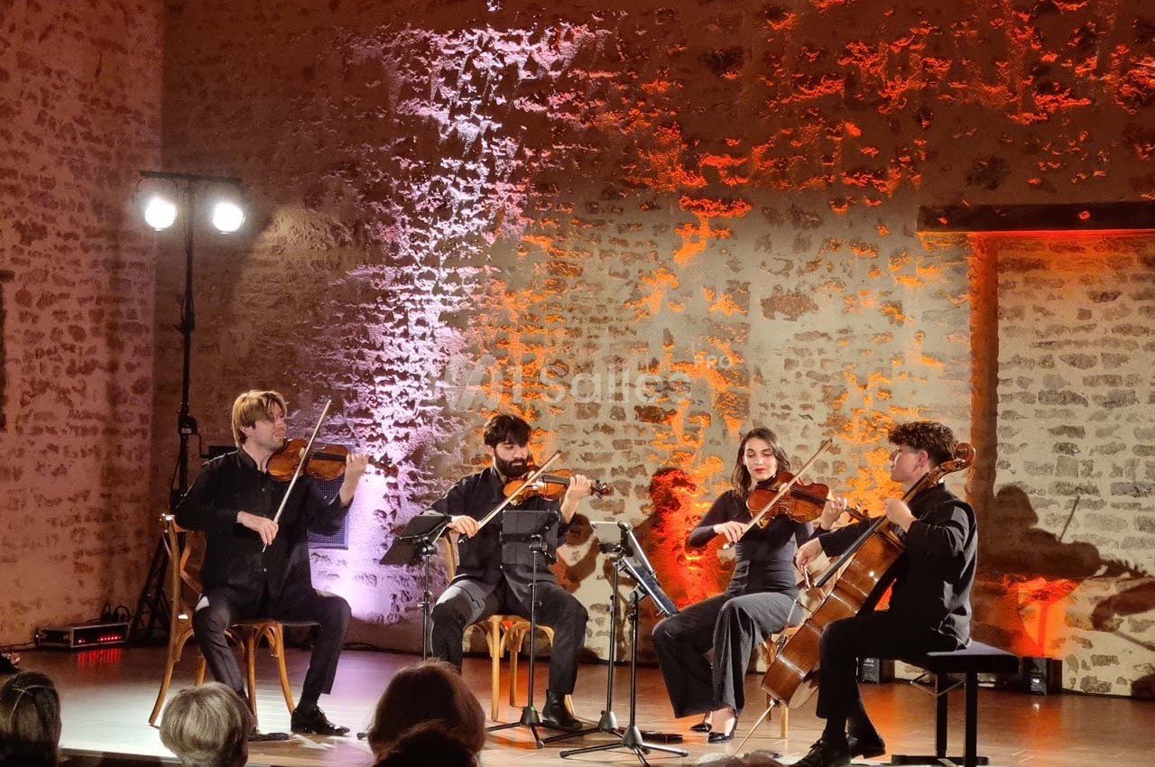 Un quatuor à cordes joue sur une scène éclairée, devant un mur en pierre avec des lumières colorées.