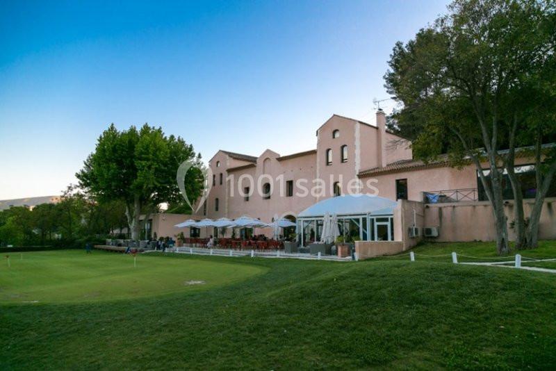 Location salle Marseille 11 (Bouches-du-Rhône) - La Bastide de la Salette #3 Bâtiment en pierre beige avec terrasse et parasols, entouré d'arbres et d'une pelouse bien entretenue.