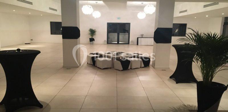 Location salle Marseille 11 (Bouches-du-Rhône) - La Bastide de la Salette #10 Salle spacieuse avec sol carrelé, tables hautes noires, poufs blancs et noirs, et plantes décoratives.