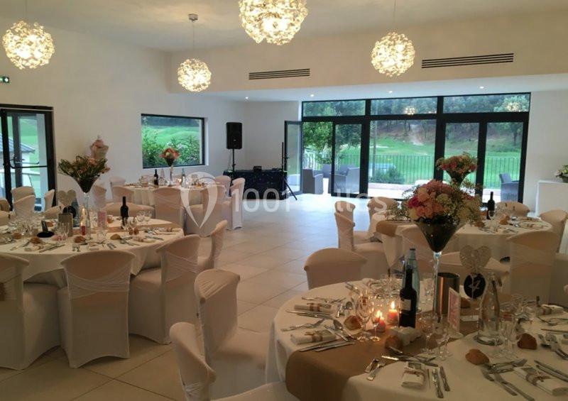 Location salle Marseille 11 (Bouches-du-Rhône) - La Bastide de la Salette #11 Salle de réception élégamment décorée avec des tables rondes dressées, des chaises blanches et une vue sur un jardin.