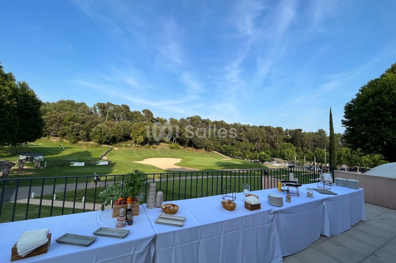 Tables dressées avec des plats et condiments en extérieur, donnant sur un terrain de golf entouré d'arbres.