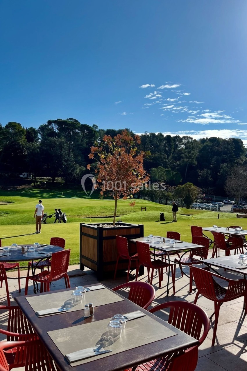 Location salle Marseille 11 (Bouches-du-Rhône) - La Bastide de la Salette #2 Terrasse d'un restaurant avec des tables vides, vue sur un terrain de golf entouré d'arbres sous un ciel ensoleillé.