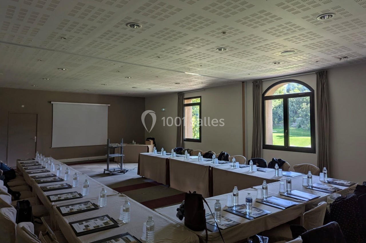 Location salle Marseille 11 (Bouches-du-Rhône) - La Bastide de la Salette #5 Salle de réunion lumineuse avec tables disposées en U, bouteilles d'eau, documents et vue sur un jardin par les fenêtres.