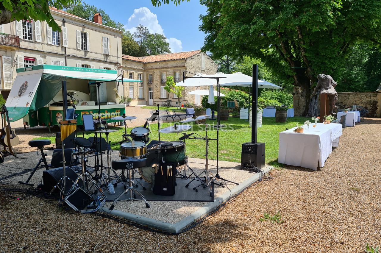 Scène extérieure avec instruments de musique, food truck et tables dressées dans un jardin devant un bâtiment ancien.