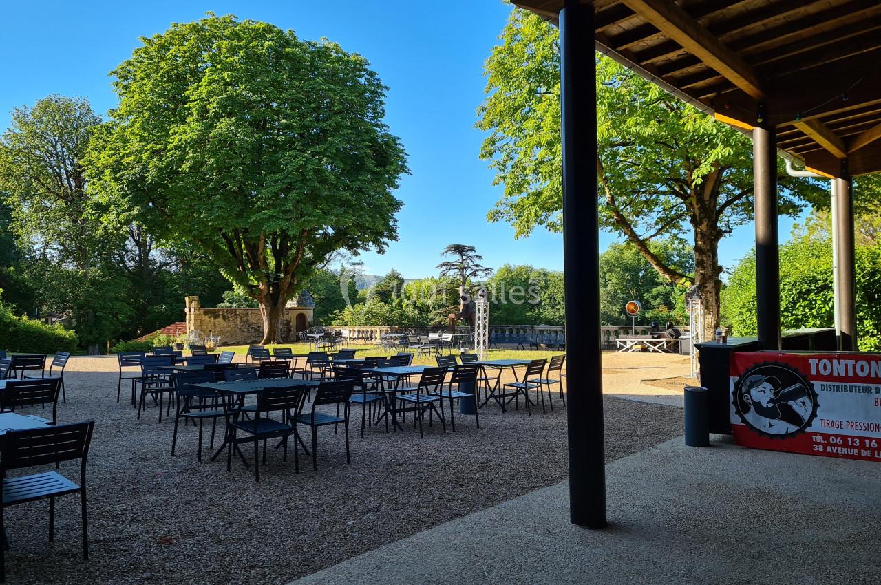 Terrasse extérieure avec tables et chaises, entourée d'arbres et d'un espace vert sous un ciel dégagé.