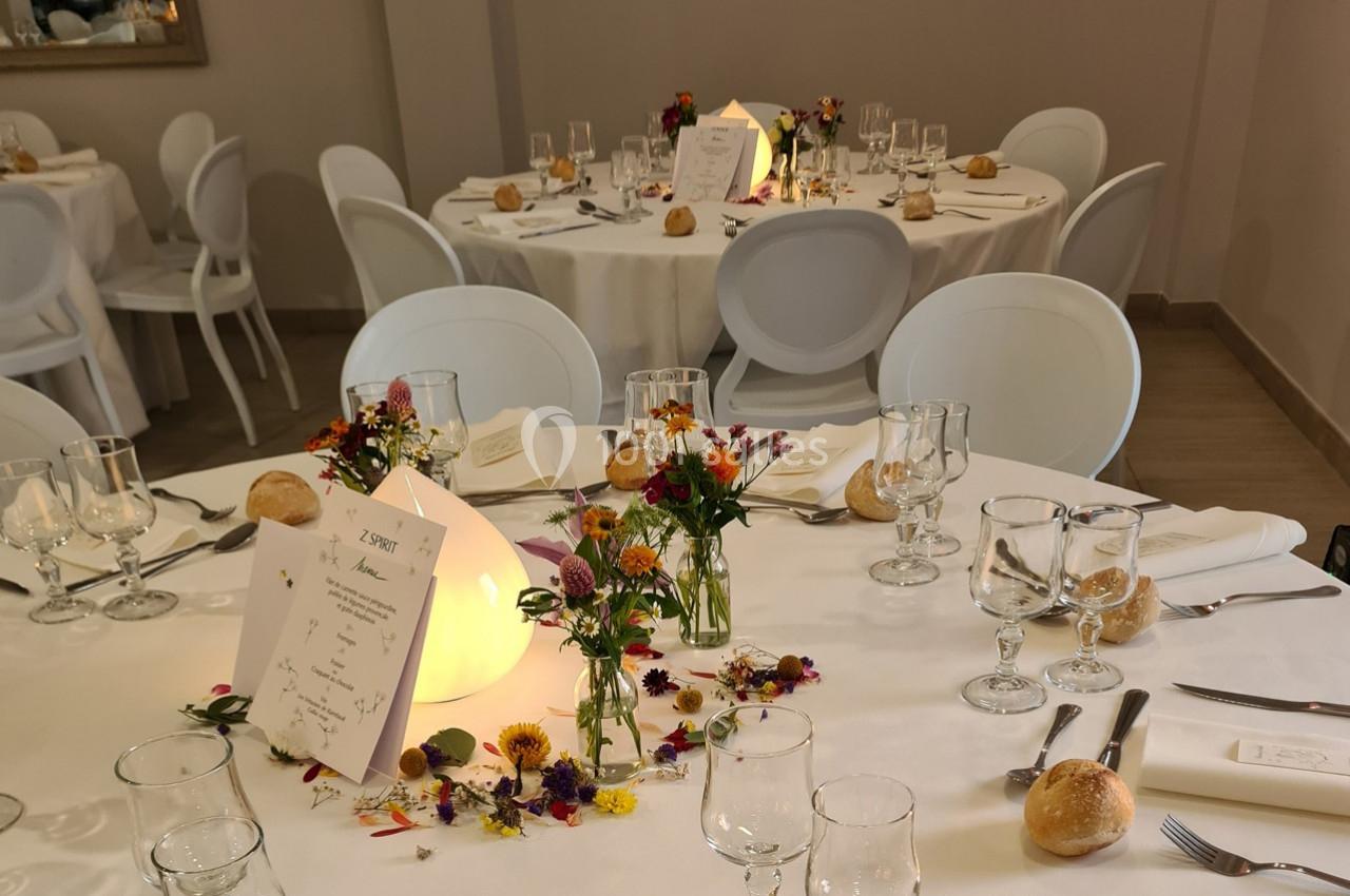 Tables de réception décorées avec des fleurs colorées, menus, verres et couverts sur nappes blanches.