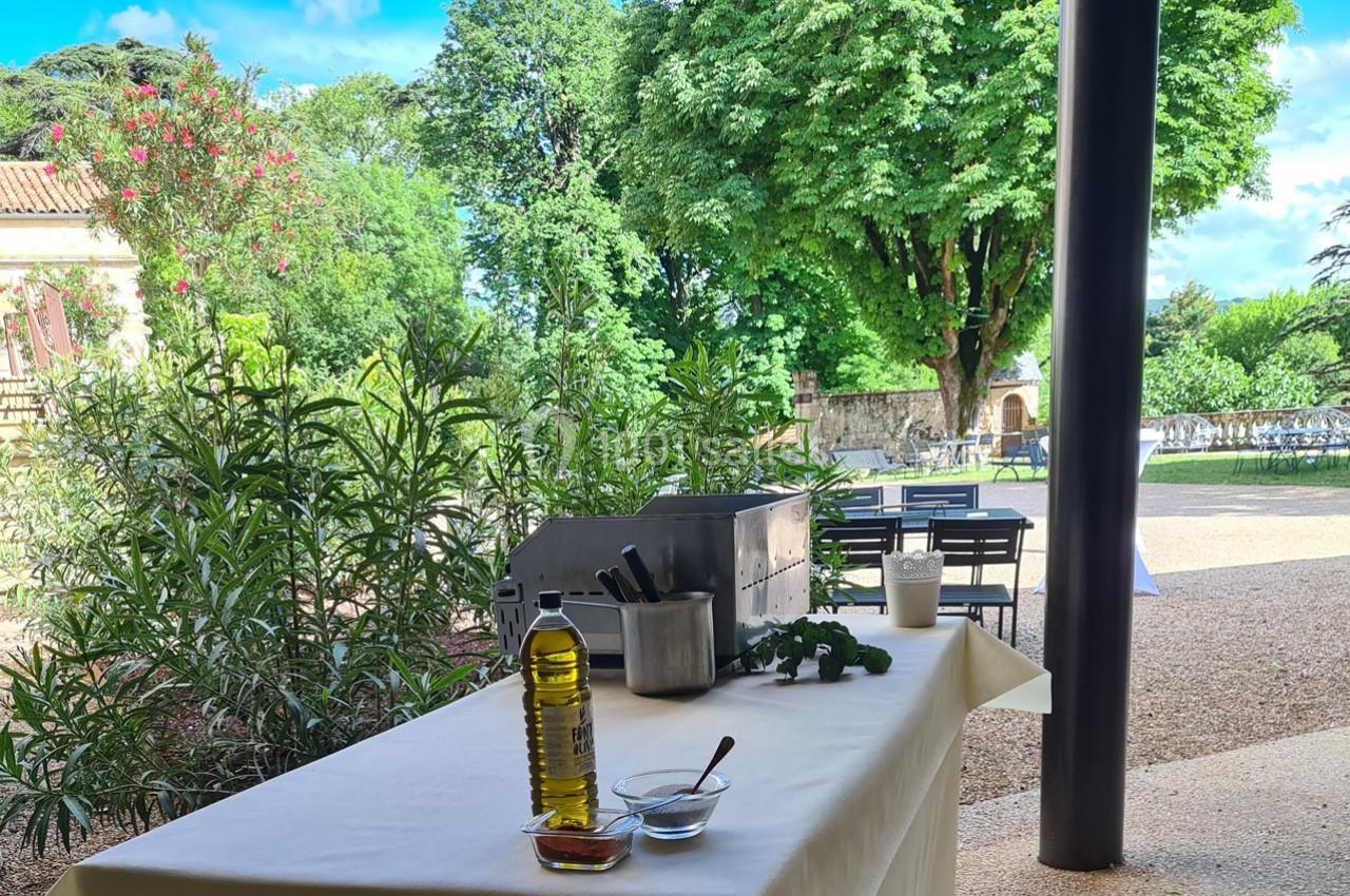 Table dressée en extérieur avec une bouteille d'huile d'olive, des herbes fraîches et des ustensiles de cuisine.