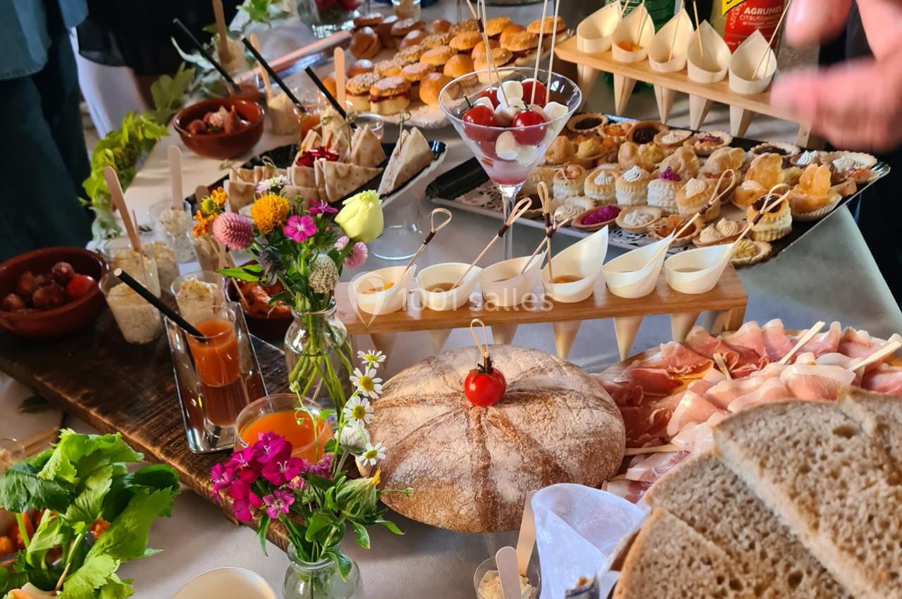 Table garnie de divers amuse-bouches, verrines, pains et fleurs décoratives lors d'un buffet.