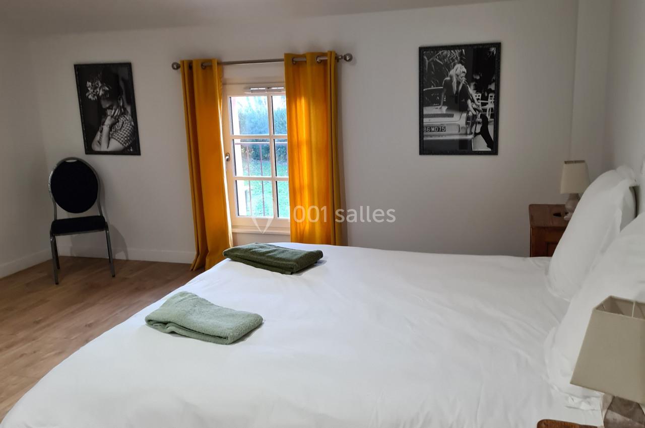 Chambre lumineuse avec lit double, draps blancs, serviettes vertes, rideaux jaunes et décorations murales en noir et blanc.