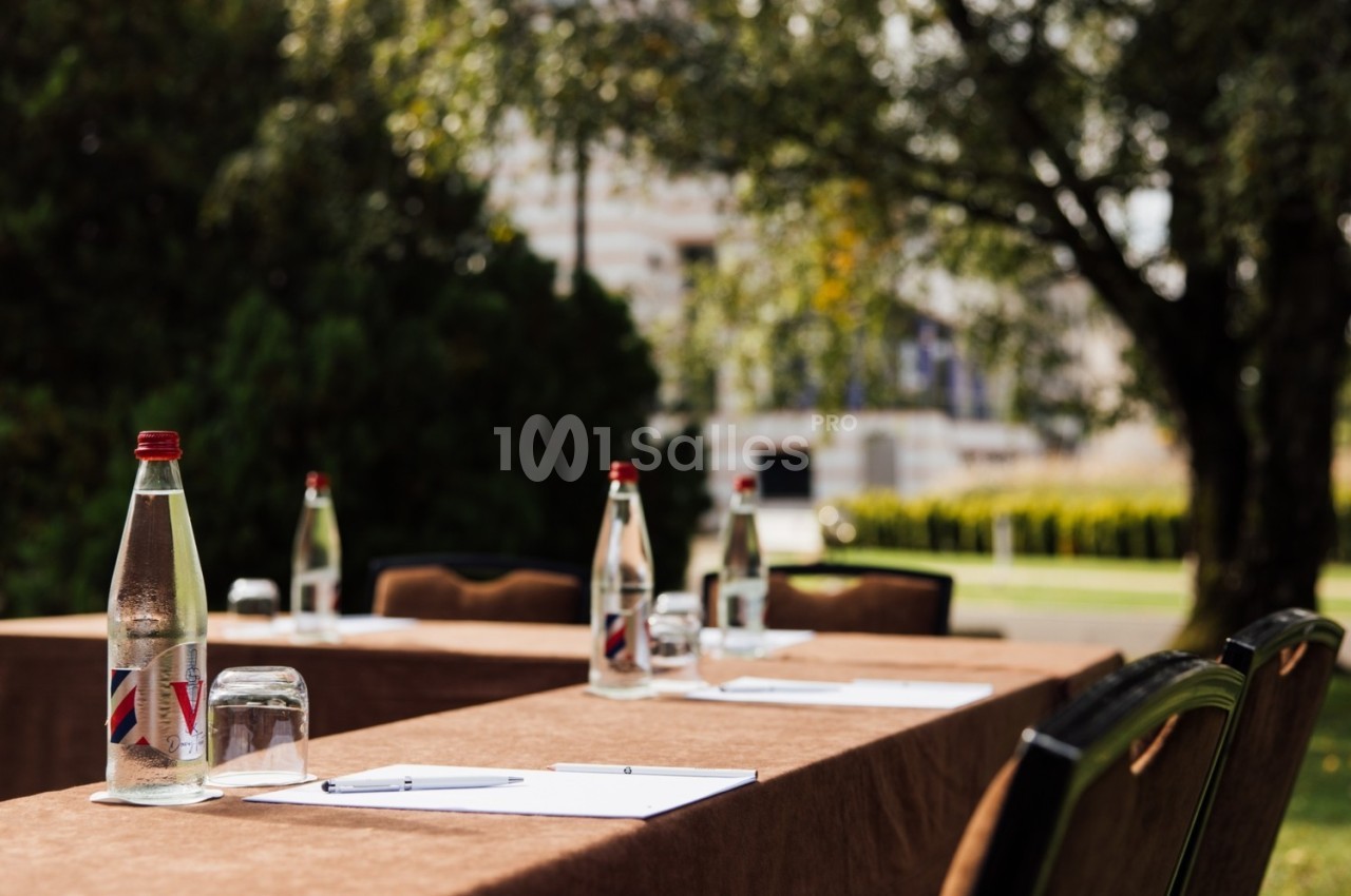 Tables en extérieur avec nappes marron, bouteilles d'eau, verres et documents, disposées pour une réunion ou un événement.
