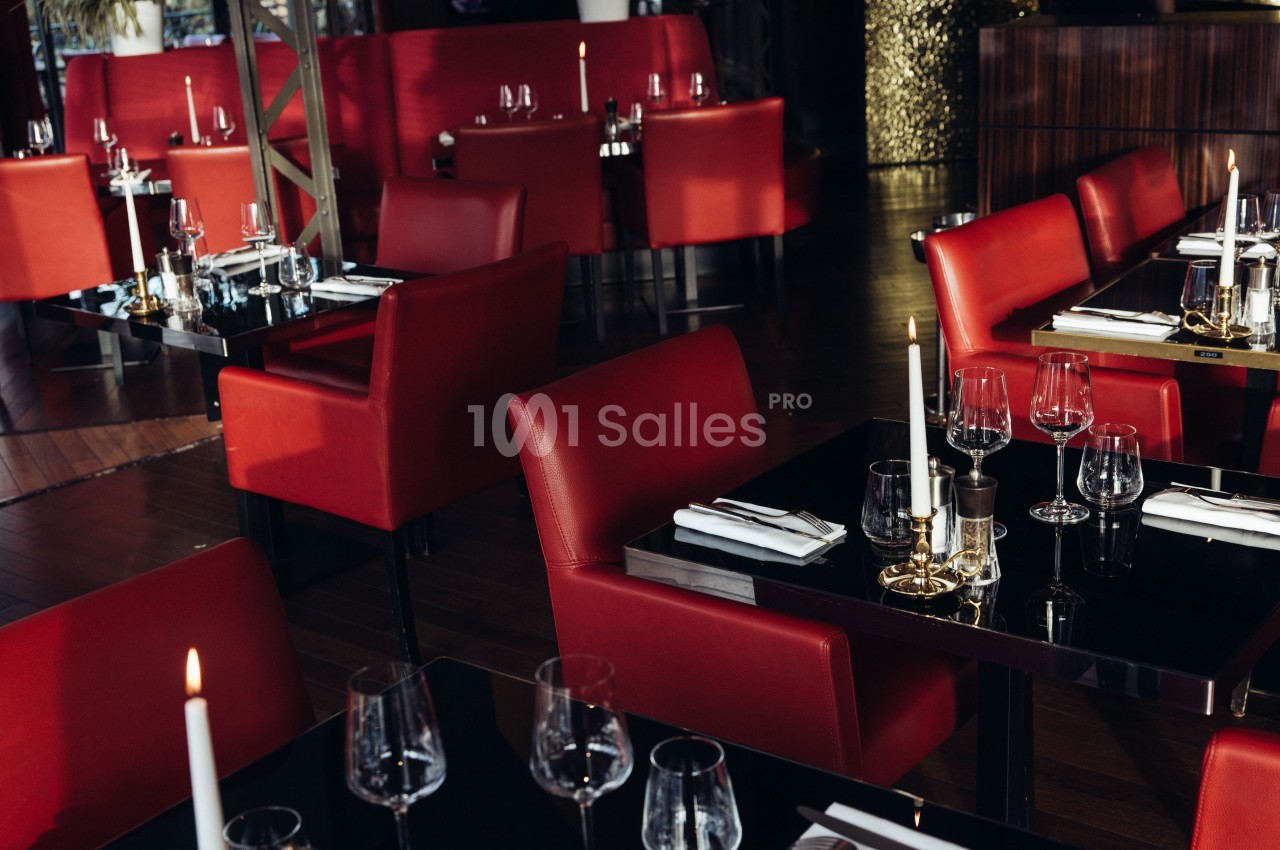 Salle de restaurant élégante avec des tables noires, des chaises rouges et des bougies allumées.