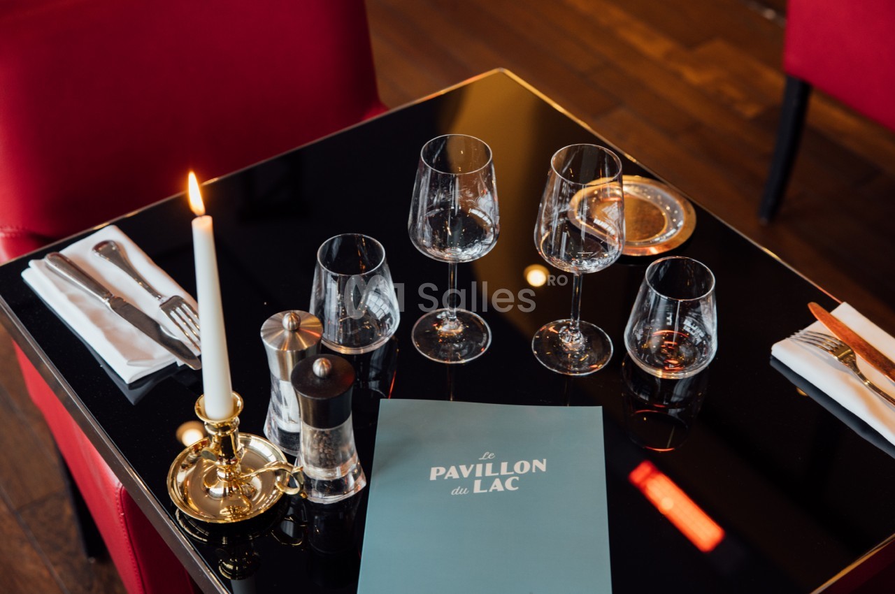 Table dressée avec des verres, couverts, une bougie allumée et un menu sur une surface noire réfléchissante.