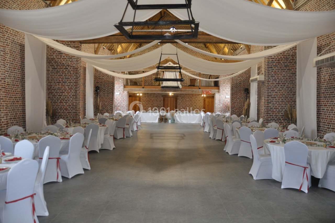 Salle de réception spacieuse avec murs en briques, tables rondes dressées et plafond décoré de voilages blancs.