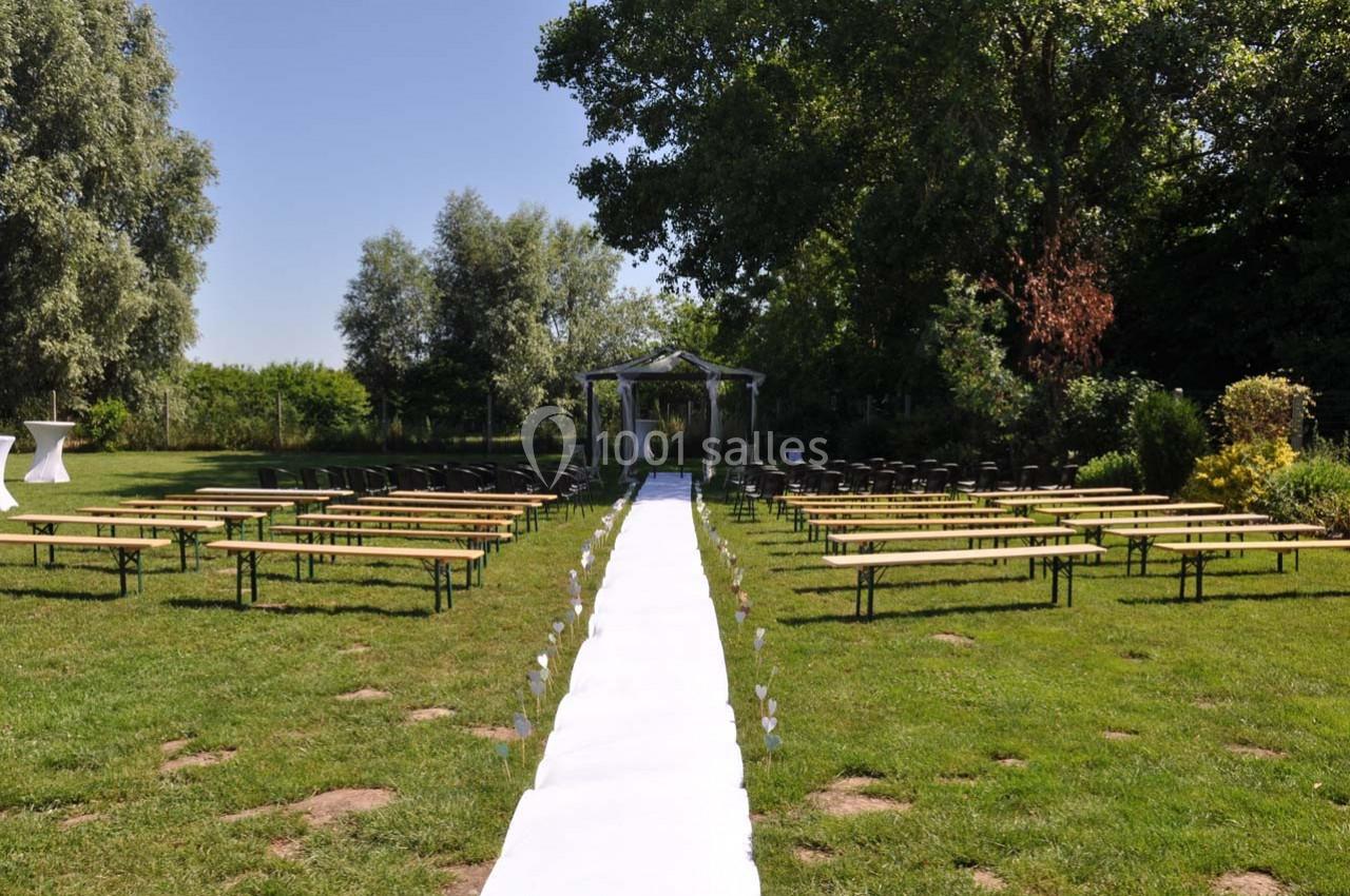 Allée centrale blanche menant à une arche décorée, entourée de bancs en bois disposés sur une pelouse verdoyante.