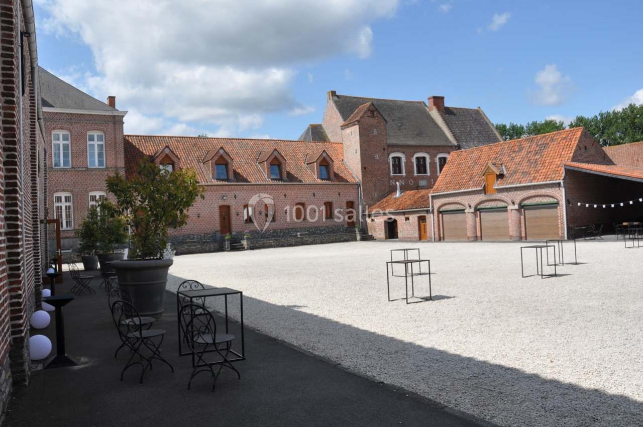 Cour pavée entourée de bâtiments en briques rouges avec tables et chaises en métal noir disposées sur le côté.