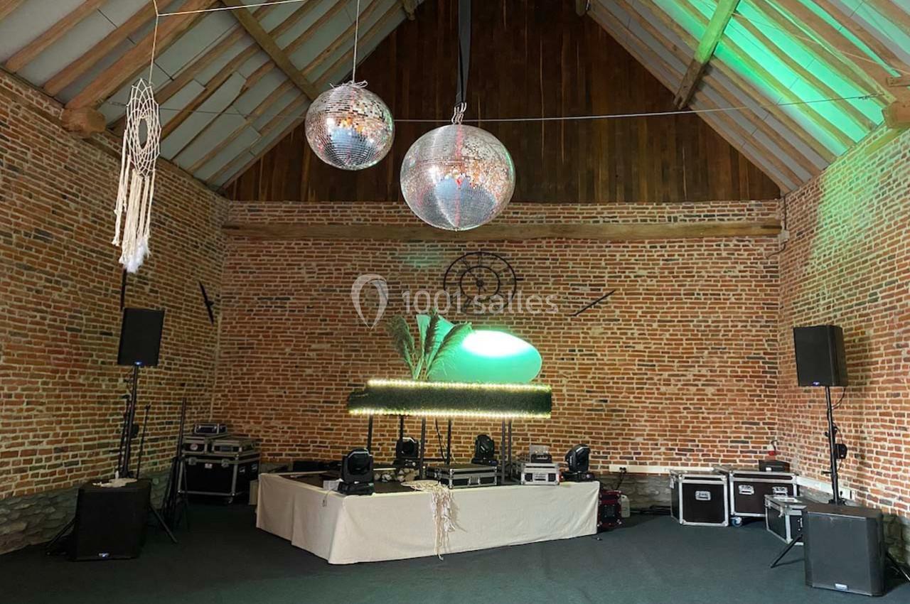 Salle en briques avec une scène équipée de matériel audio, décorée de boules à facettes et d'éléments bohèmes.